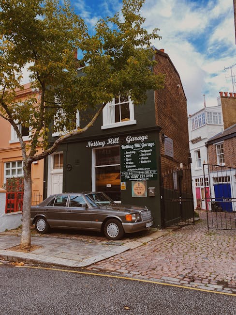 A two-story brick building on a cobblestone street housing Notting Hill Garage, a garden maintenance and landscaping service in Notting Hill. The building has a dark green facade with a large window a